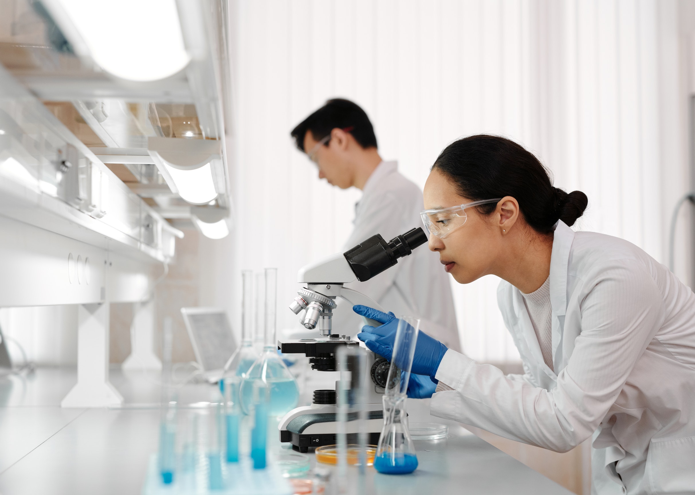Two physicians inside of a lab. The physicians are wearing white lab coats and are analyzing test samples.